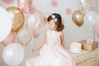 Altı yaşında açık pembe elbiseli bir kız evde doğum gününü kutluyor..