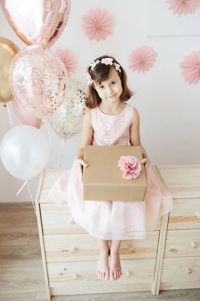 Altı yaşında açık pembe elbiseli bir kız evde doğum gününü kutluyor..