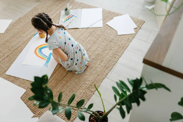 Child lying on floor and hold her draw with rainbow — Stock Photo, Image