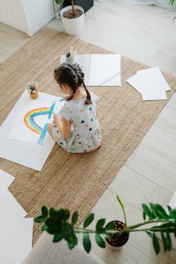 Çocuk yerde yatıyor ve çizimini gökkuşağıyla yapıyor.