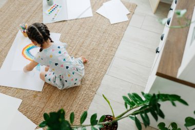 Çocuk yerde yatıyor ve çizimini gökkuşağıyla yapıyor.