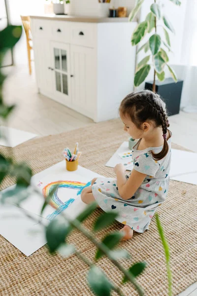 Çocuk yerde yatıyor ve çizimini gökkuşağıyla yapıyor.