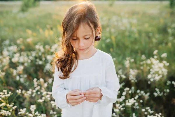 Summer vibes. The feeling of summer. Portrait of cute little girl wearing white blouse in the fields having cherries earrings