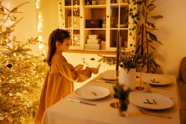 Christmas decorated dining table with dishes, glasses and candles, serving. Young girl light candles