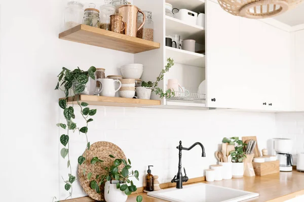 View on white simple modern kitchen in scandinavian style, kitchen details, houseplants in interior, wooden table, white ceramic brick wall background