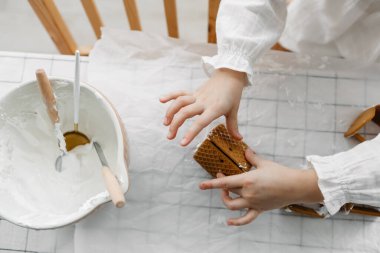Adorable brown-haired girl wearing white blose decorate with icing gingerbread houses at the kitchen. Christmas sweets, popular Christmas decorations. Gingerbread house - classic holiday tradition
