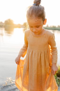 Portrait of cute caucasian girl wearing natural linen dress, lake water in sunset light background, summertime. Coutryside living. Summer vibes. The feeling of summer.