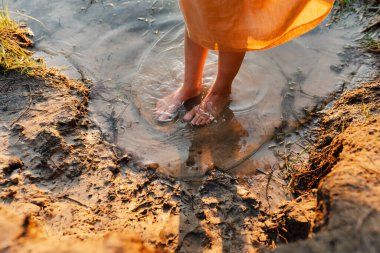 Feets of girl wearing natural linen dress standing in lake water, summertime. Coutryside living. Summer vibes. The feeling of summer.