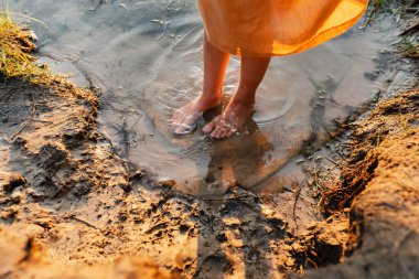 Feets of girl wearing natural linen dress standing in lake water, summertime. Coutryside living. Summer vibes. The feeling of summer. clipart
