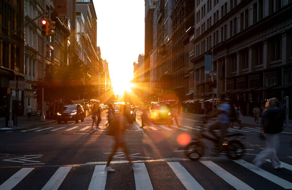 Sunlight light fades behind the buildings on 23rd Street with busy crowds of people and cars crossing the intersection in New York City NYC