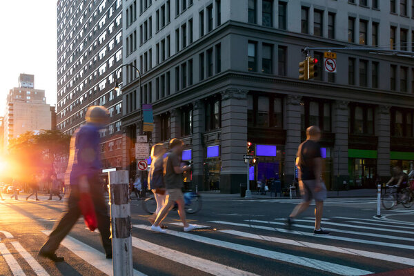 Busy intersection with people walking through the crosswalk on 14th Street and 5th Avenue in New York City with sunlight background