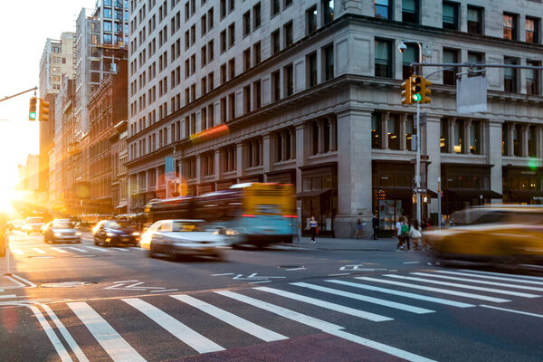 Busy intersection on 5th Avenue and 23rd Street in New York City with rush hour traffic driving into the sunset NYC
