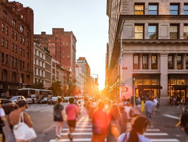 People walking through the busy intersection at 5th Avenue and 23rd Street in New York City with sunlight shining in the background