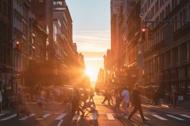 Busy intersection with crowds of people walking across the intersection at 23rd Street and 5th Avenue in New York City with sunset light shining in the background