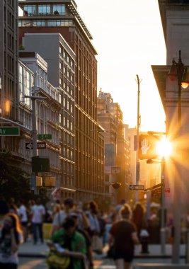 Crowds of people walking down the busy street with sunlight shining between the background buildings