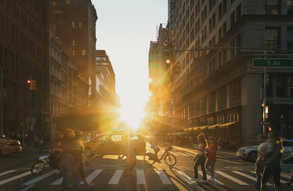 People, bikes and taxis in a busy intersection on 5th Avenue in New York City with the light of sunset shining in the background