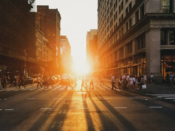 Sunlight shining on the diverse crowds of people walking across the busy intersection on 5th Avenue in New York City NYC