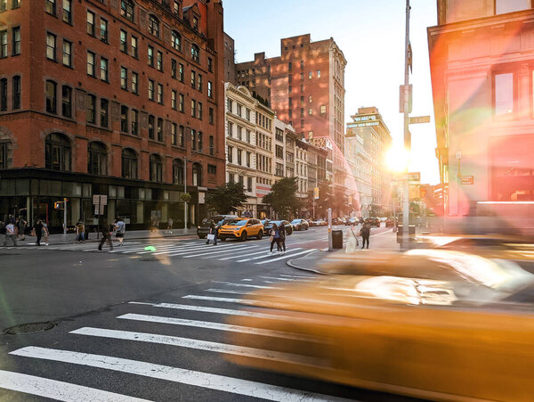 Blurred yellow taxis driving through the intersection of 23rd Street and 5th Avenue in New York City with sunlight shining in background