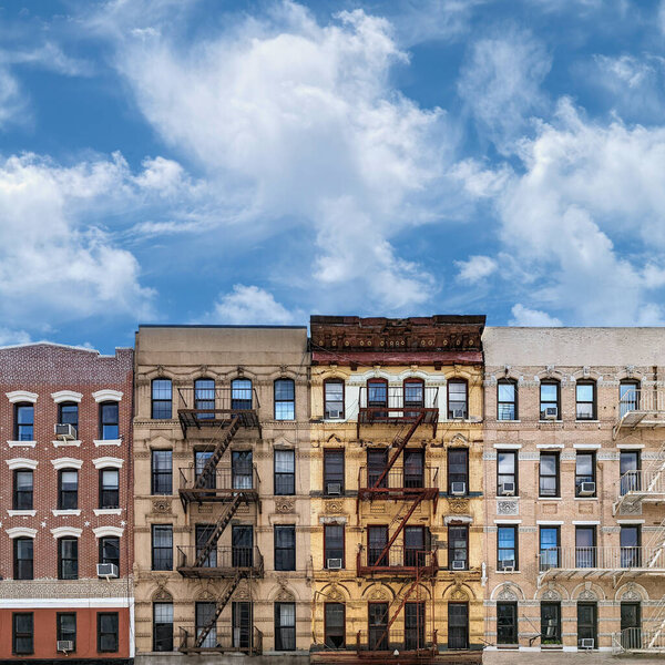 Old apartment buildings in New York City with fluffy white clouds in the blue sky background above