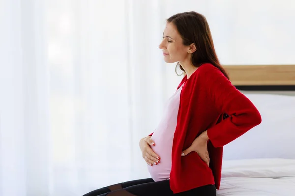 Pregnant Woman Sits Bed Bedroom Holding Her Back Showing Pain — Stockfoto