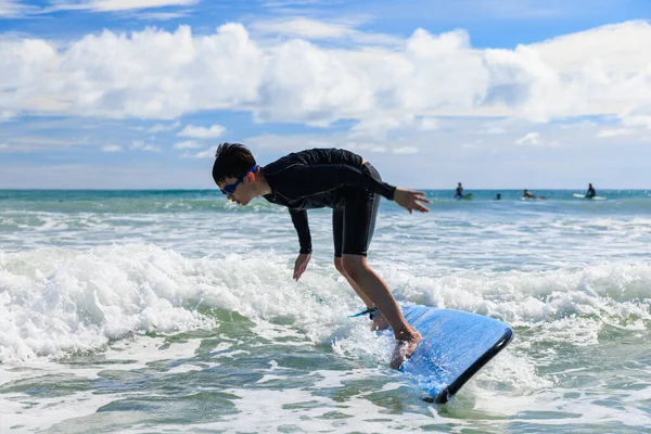 Young boy, new student in surfing, loses his body balance and falls from surfboard into the water during class. The concept of practice and perseverance before it succeeds.