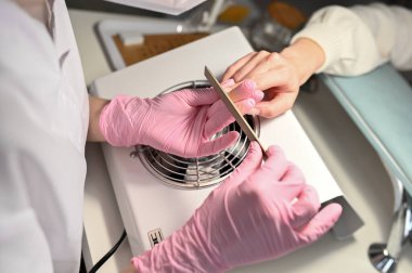 A woman is getting a manicure for her nails. Beautician file nails to client.