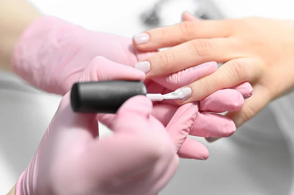 Manicurist in pink gloves paints nails with nail polish