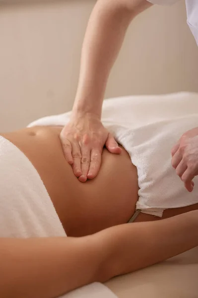Woman receiving a belly massage at spa salon. Female patient is receiving treatment by professional osteopathy therapis