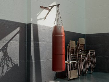 A red leather punching bag mounted on a wall in a room with stacked chairs lit by a window light - 3D render clipart