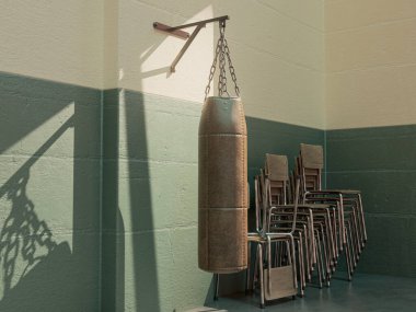 A old vintage leather punching bag mounted on a green wall in a room with stacked chairs lit by a window light - 3D render clipart
