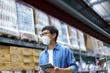 Yeni normal Asyalı adamlar, personel, yüz maskesi takan ürünler. Depo Kontrol Müdürü 'nü de sayarsak depodaki ürünleri sayıyor ve denetliyor.