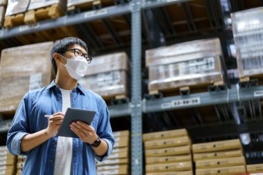 Yeni normal Asyalı adamlar, personel, yüz maskesi takan ürünler. Depo Kontrol Müdürü 'nü de sayarsak depodaki ürünleri sayıyor ve denetliyor.