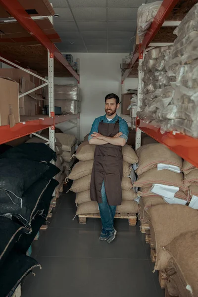 Warehouse worker standing near bags with coffee beans in the coffee small factory