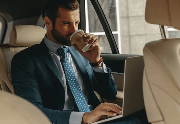 Waist up portrait of business man in formal wear drinking beverage while sitting in a car