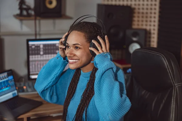 Cheerful funny African woman presenter smiling while putting on headphones, ready to speak with listeners. Broadcasting, radio, music recording studio concept