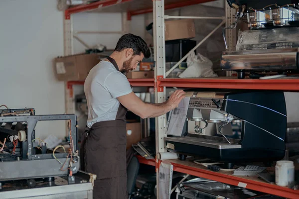 Man worker in uniform inspecting coffee machine in own workshop. High quality photo