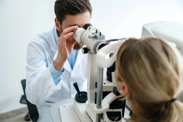 Optometrist with non-contact tonometer checks the patients intraocular pressure in opticians shop