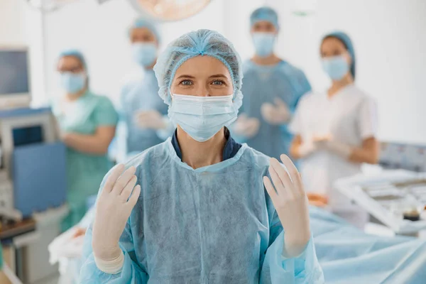 Female surgeon standing in operating room, ready to work on patient on background of colleagues