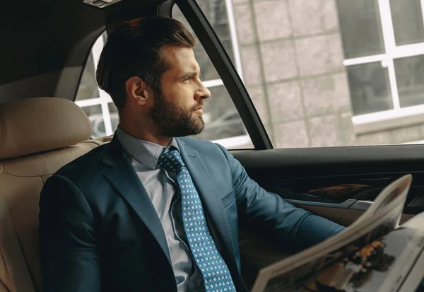 Close up side view portrait of handsome Caucasian man in formal wear look to the outside while sitting in a car
