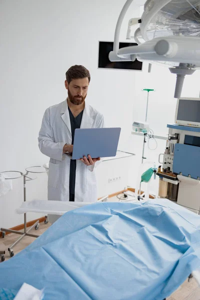 Professional doctor standing with laptop before operation in modern clinic. High quality photo