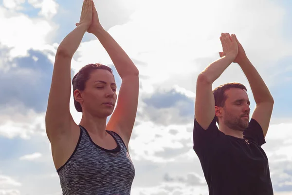 Young healthy man and woman doing yoga in the sunny summer park. High quality photo