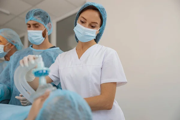 Nurse holding breathing mask on patient face during operation in clinic. Withdrawal from anesthesia