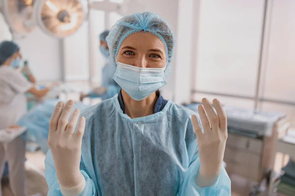 Female surgeon standing in operating room, ready to work on patient on background of colleagues