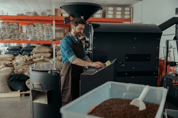 Smiling Business owner operating of coffee roasting machine on own small roasted factory