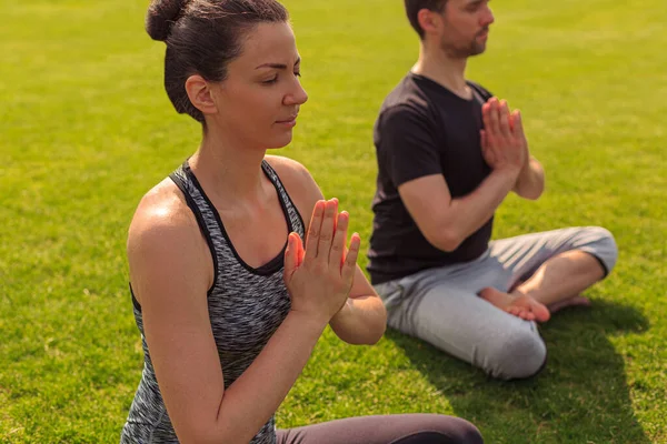 Young healthy man and woman doing yoga in the sunny summer park. High quality photo