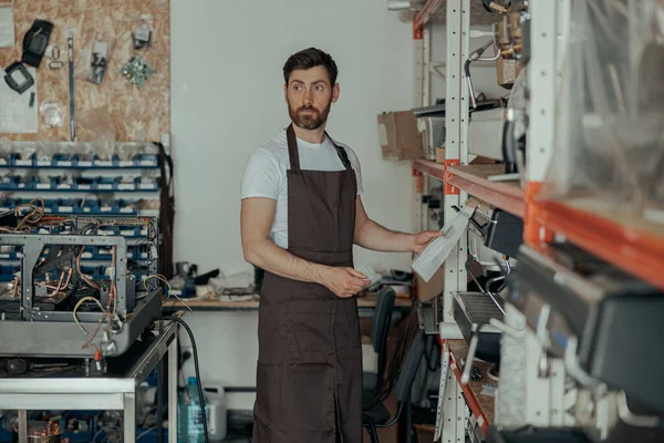 Man worker in uniform inspecting coffee machine in own workshop. High quality photo