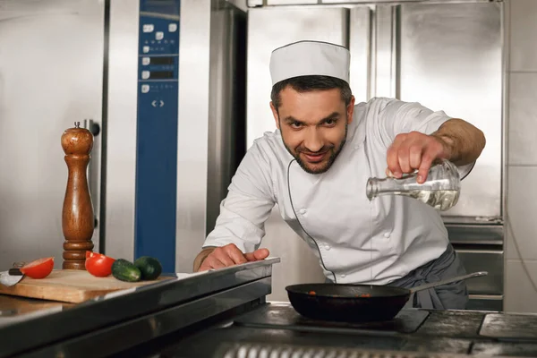 Chef pours oil into frying pan for preparing dish on restaurant kitchen. High quality photo