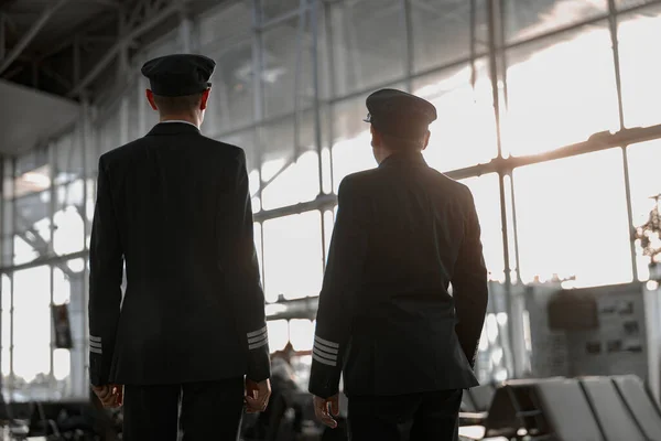 Back view of two male pilots posing in airport terminal