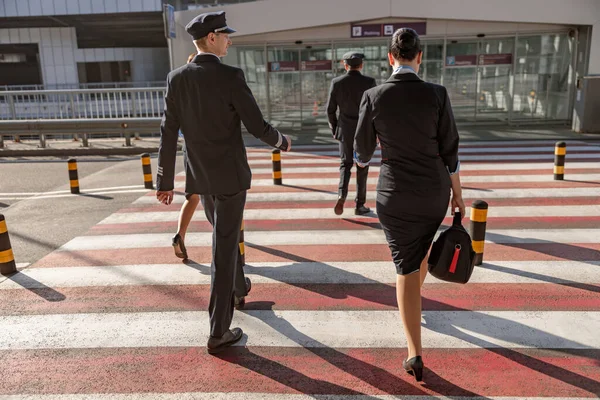 Back view of pilots and flight attendants crossing the road to the terminal outdoors