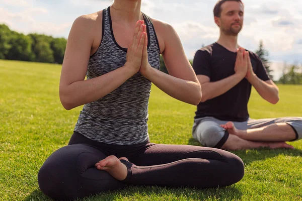 Young healthy man and woman doing yoga in the sunny summer park. High quality photo